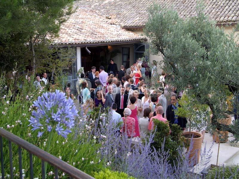 Groupe de personnes rassemblées dans un jardin fleuri près d'une maison au toit de tuiles.