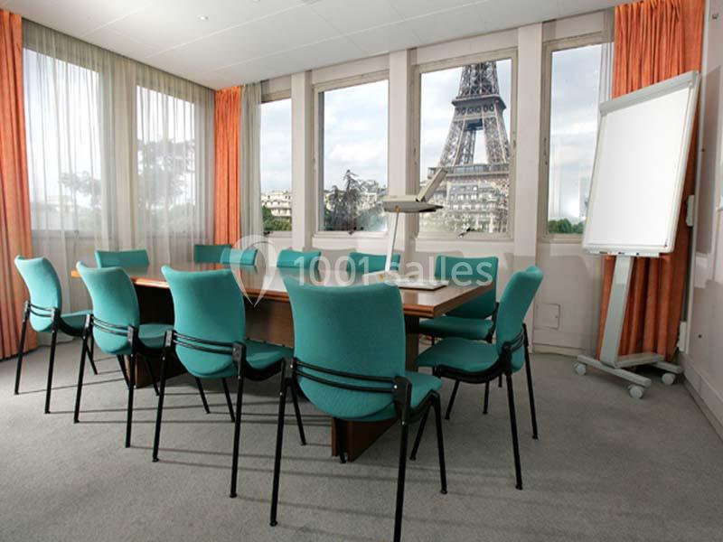Salle de réunion avec table, chaises turquoise, tableau blanc et vue sur la tour Eiffel par les fenêtres.