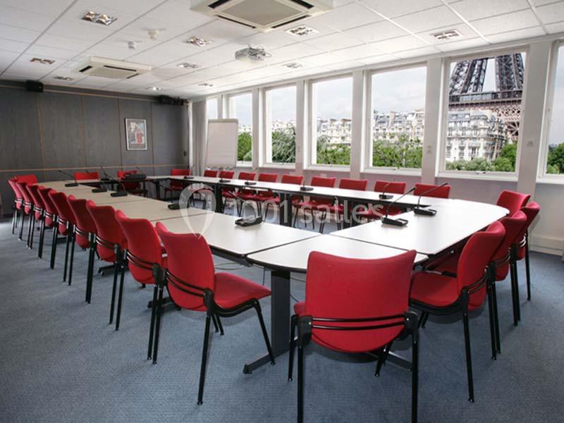 Salle de réunion lumineuse avec des chaises rouges, des tables blanches et vue sur la Tour Eiffel par les fenêtres.