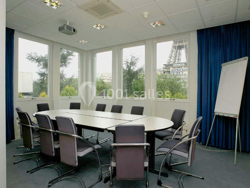 Salle de réunion lumineuse avec table ovale, chaises, paperboard et vue sur la Tour Eiffel à travers de grandes fenêtres.