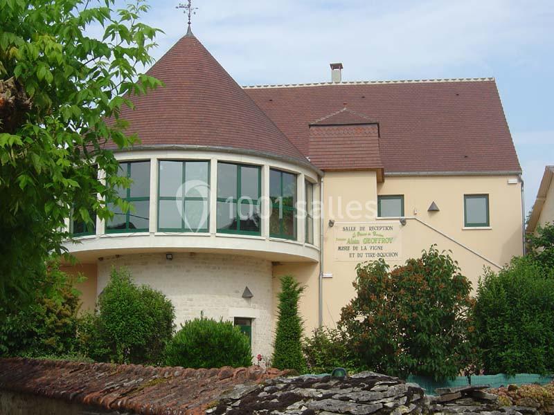Bâtiment avec toit en tuiles rouges, grande baie vitrée arrondie et panneau indiquant une salle de réception.