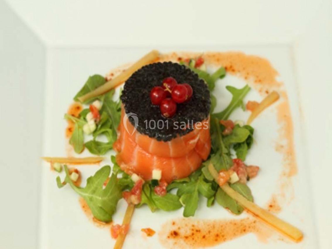 Assiette de saumon fumé enroulé, garni de caviar et groseilles, sur un lit de roquette avec une sauce colorée.