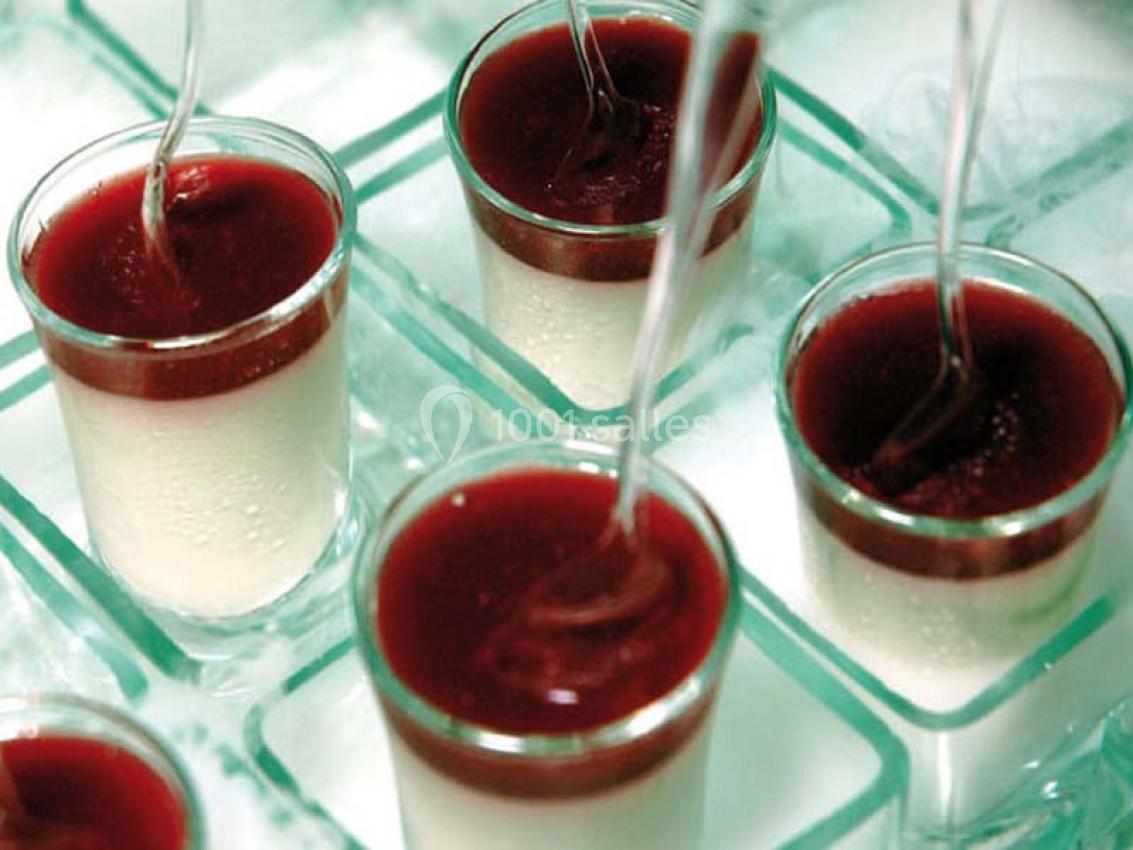 Verres individuels de panna cotta garnis d'un coulis rouge, disposés sur un plateau avec des cuillères transparentes.