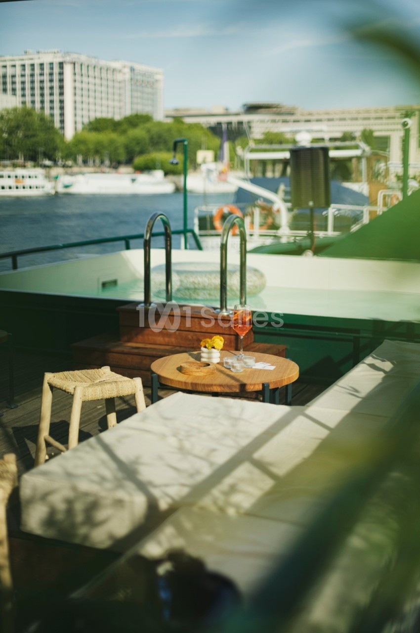 Table en terrasse avec boissons et fruits, vue sur la Seine et bâtiments en arrière-plan par une journée ensoleillée.