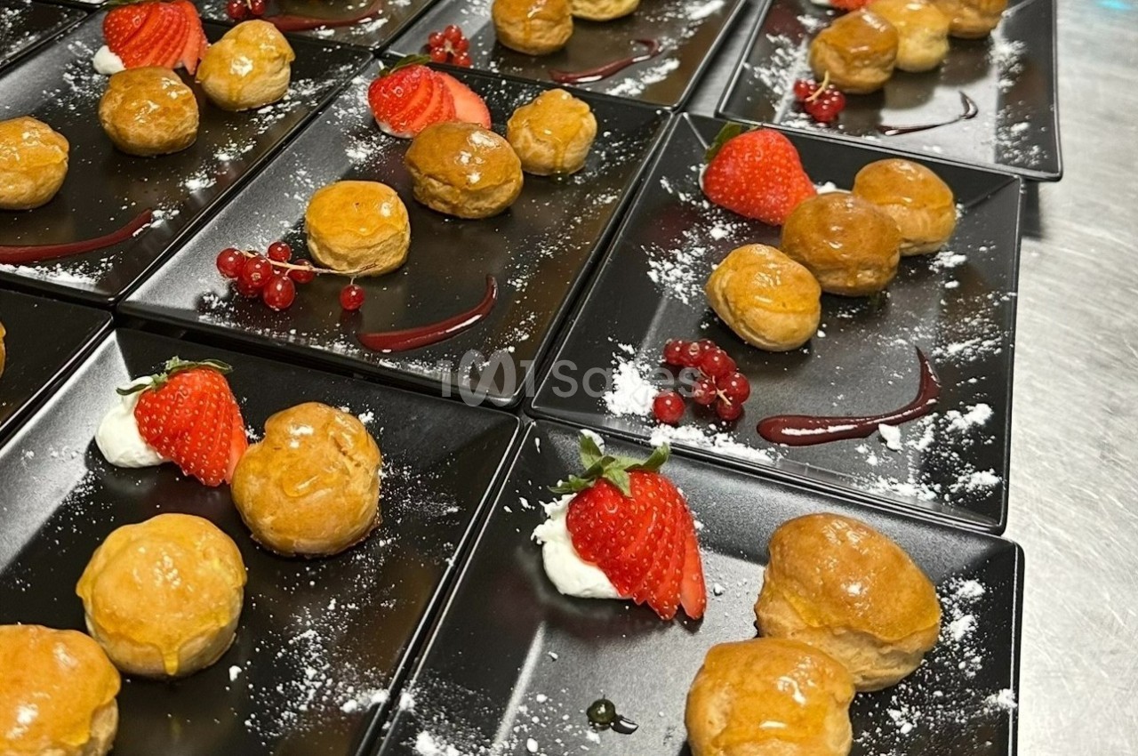 Assiettes noires garnies de choux dorés, fraises, groseilles, crème et filet de coulis rouge.