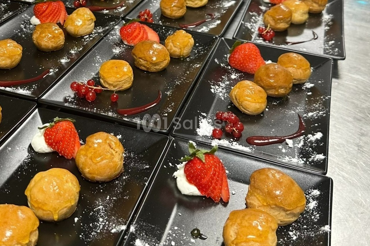 Assortiment de desserts avec choux glacés, fraises, groseilles et crème, présentés sur des assiettes noires.