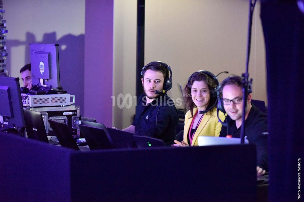 Des techniciens et une femme souriante travaillent sur des ordinateurs et équipements audio dans une régie technique.