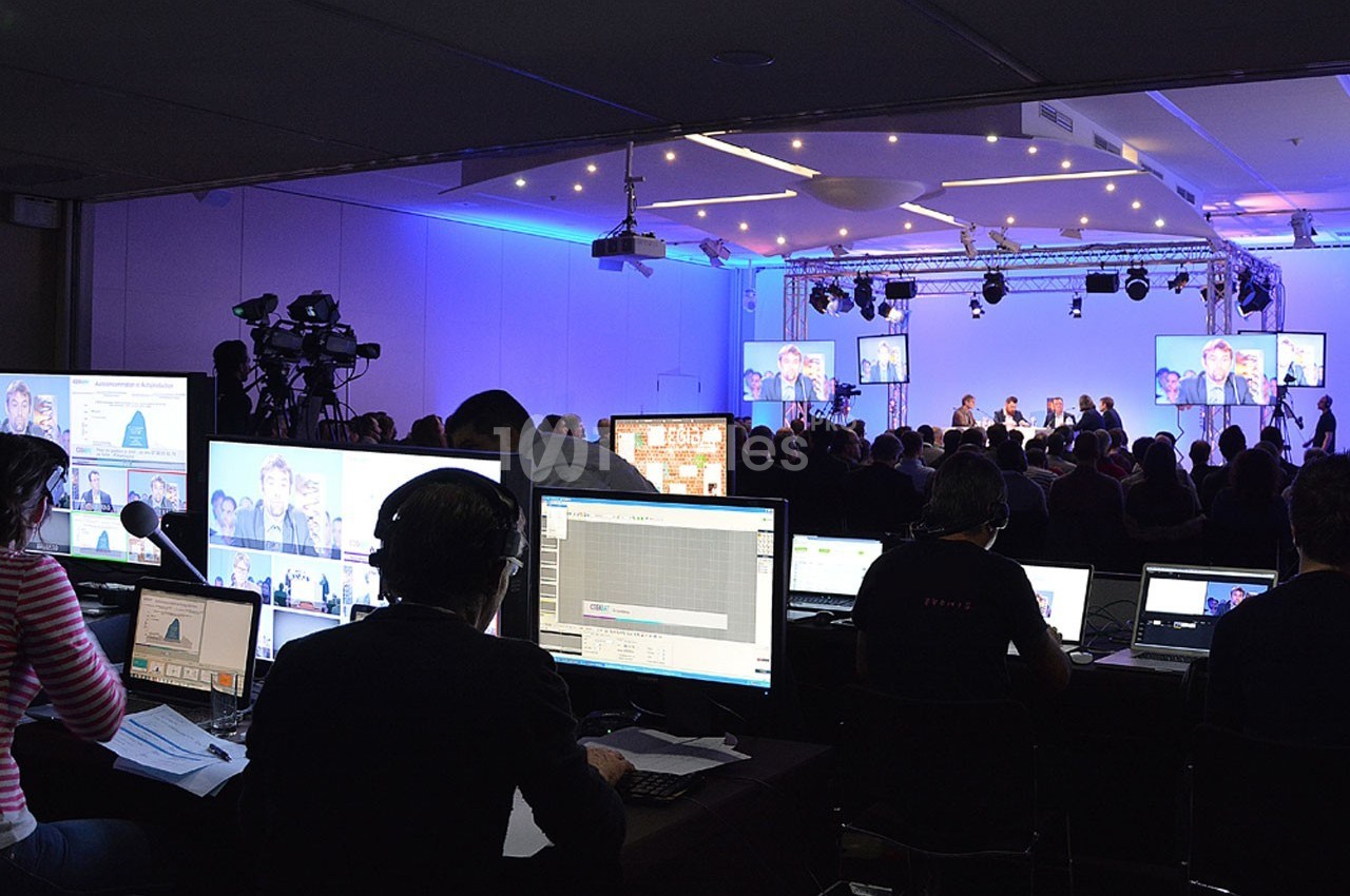 Des techniciens gèrent des équipements audiovisuels lors d'une conférence avec des intervenants sur scène.