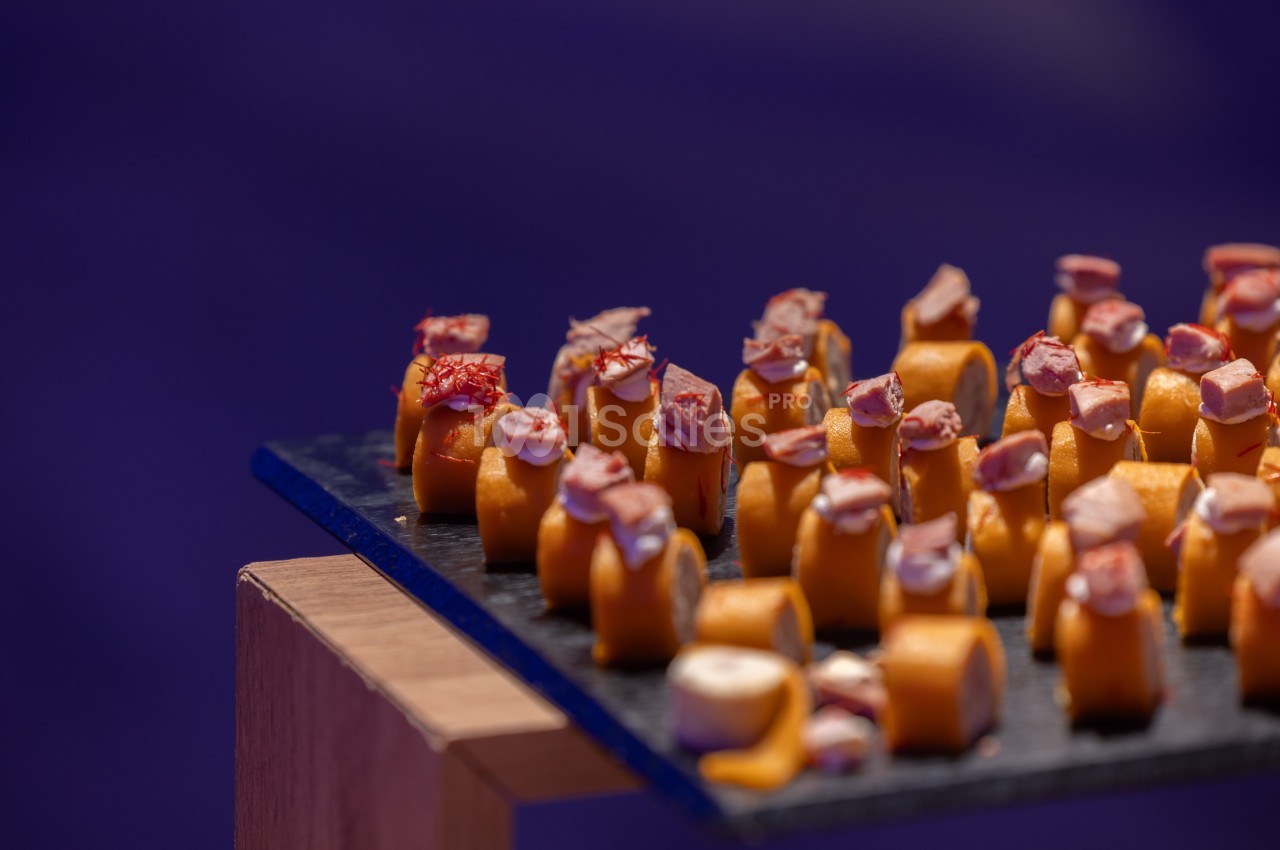 Assortiment de bouchées apéritives disposées sur une ardoise noire, avec un fond violet flou.