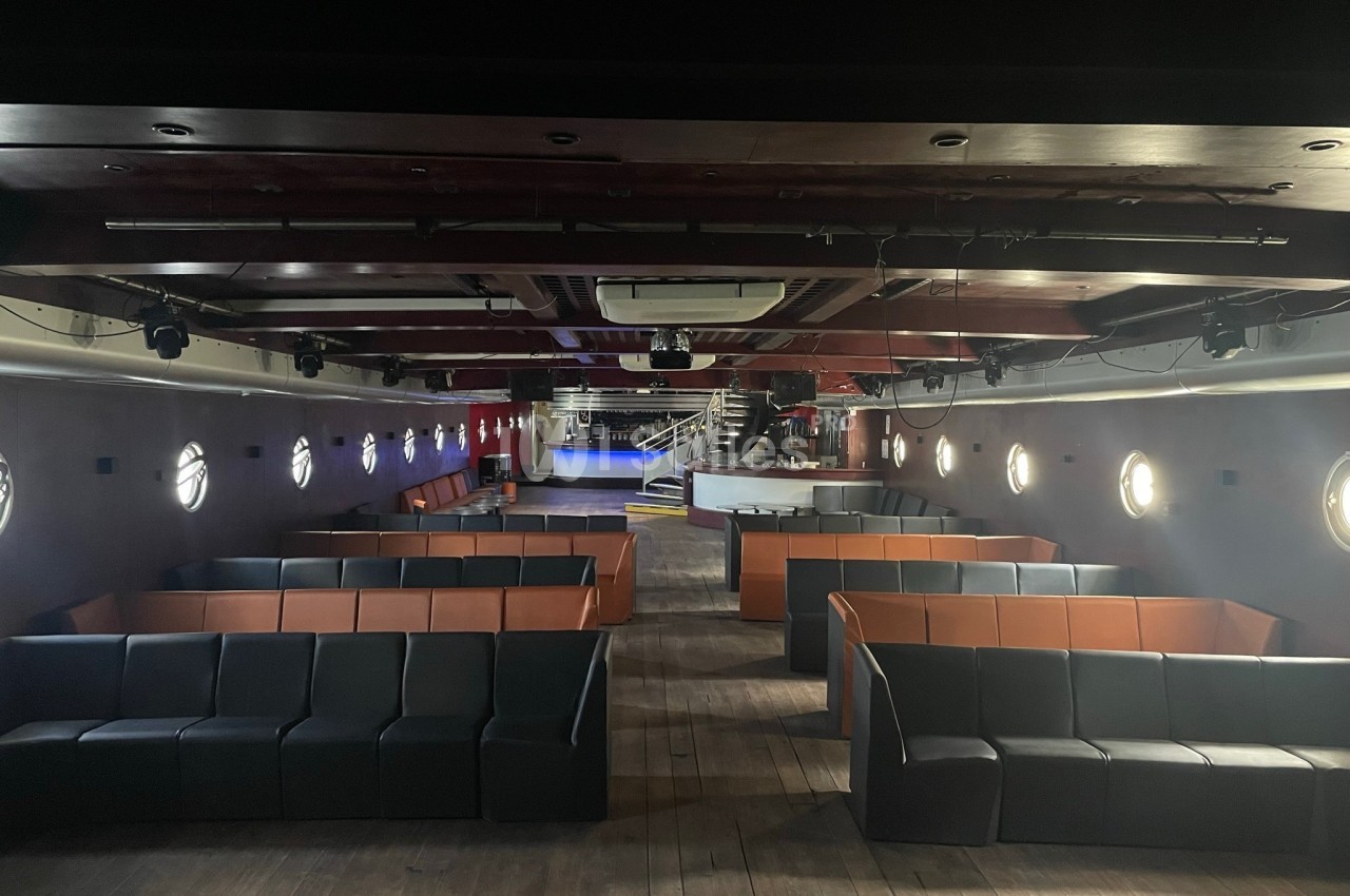 Salle de réception avec banquettes noires et oranges, bar surélevé, scène, éclairage encastré et spots directionnels.