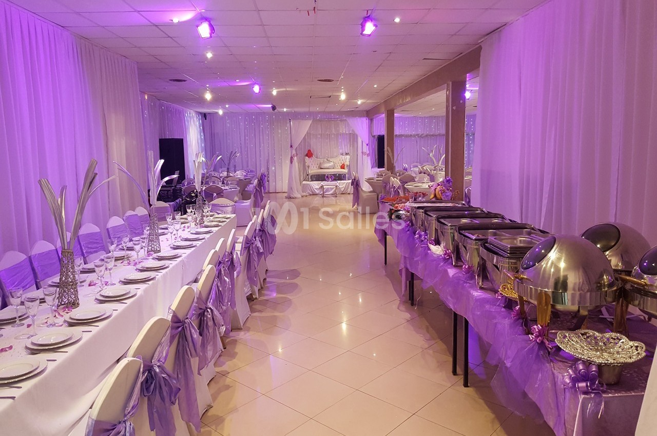 Salle de réception décorée en violet avec tables dressées et buffet disposé sur le côté.