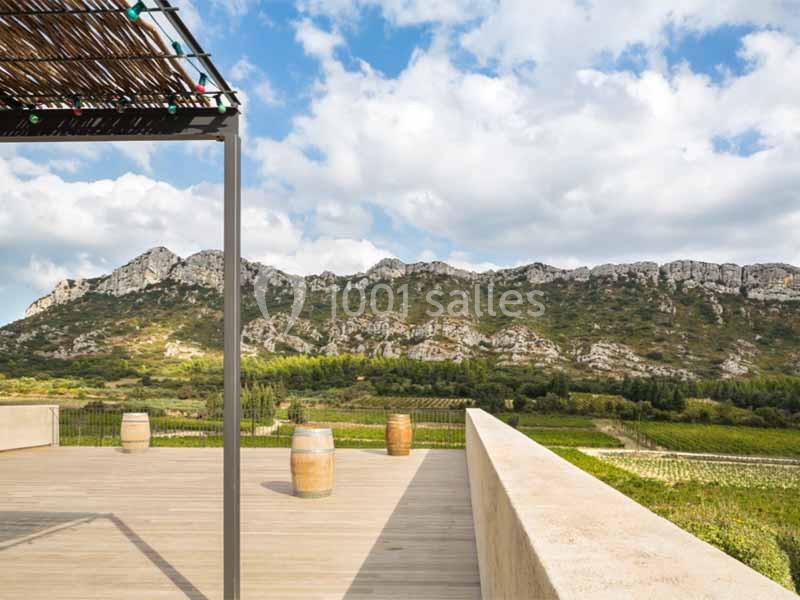 Terrasse en bois avec vue sur des vignes et des montagnes sous un ciel partiellement nuageux.