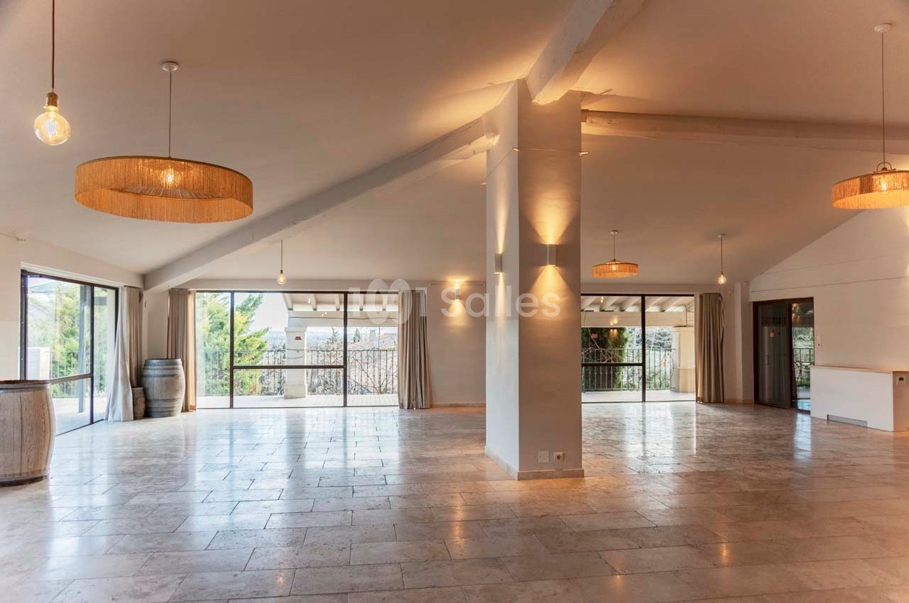 Salle spacieuse et lumineuse avec de grandes baies vitrées, un sol en pierre et des suspensions en osier.