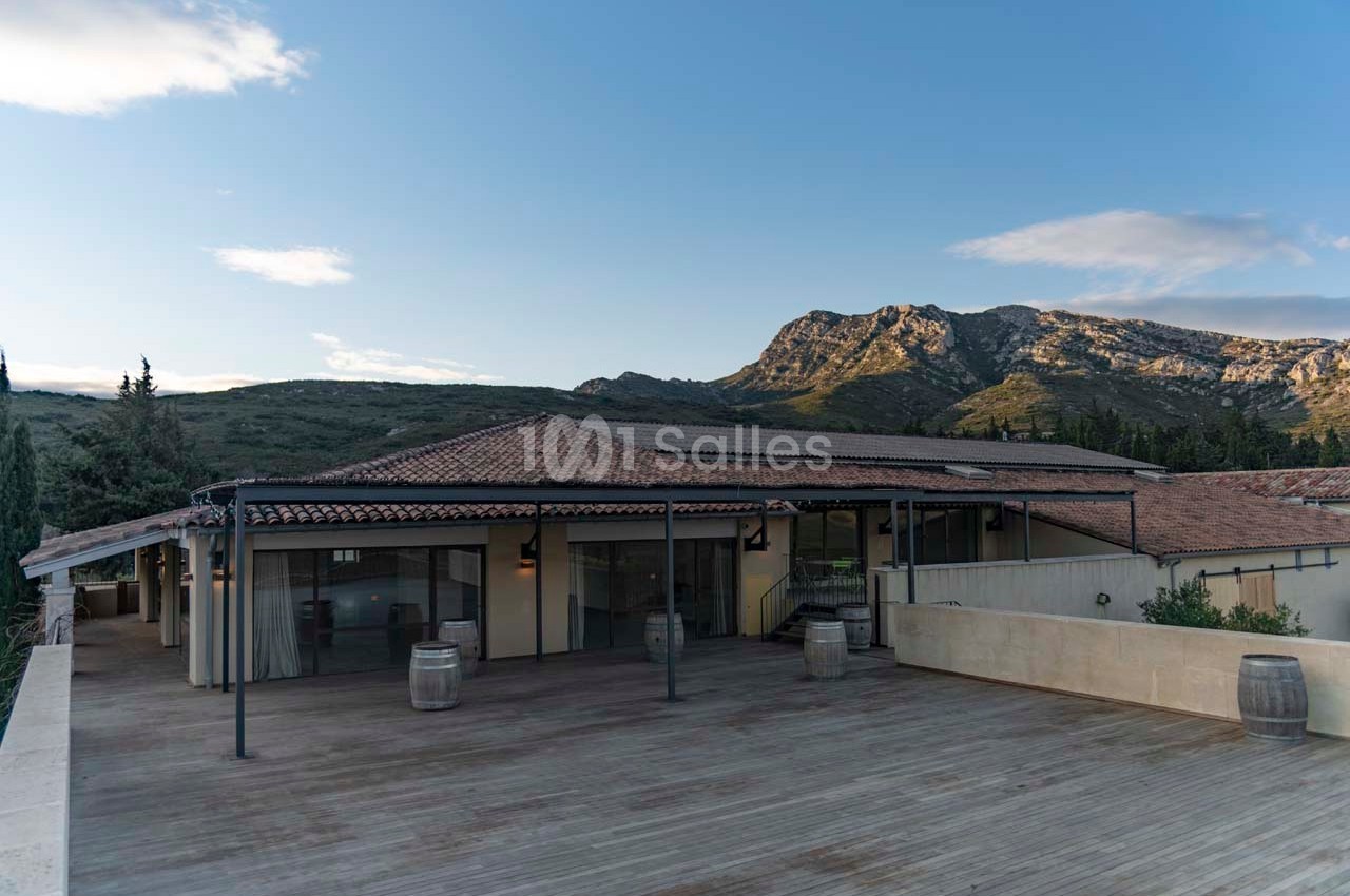 Terrasse en bois avec vue sur un bâtiment à toit en tuiles, entourée de collines sous un ciel dégagé.