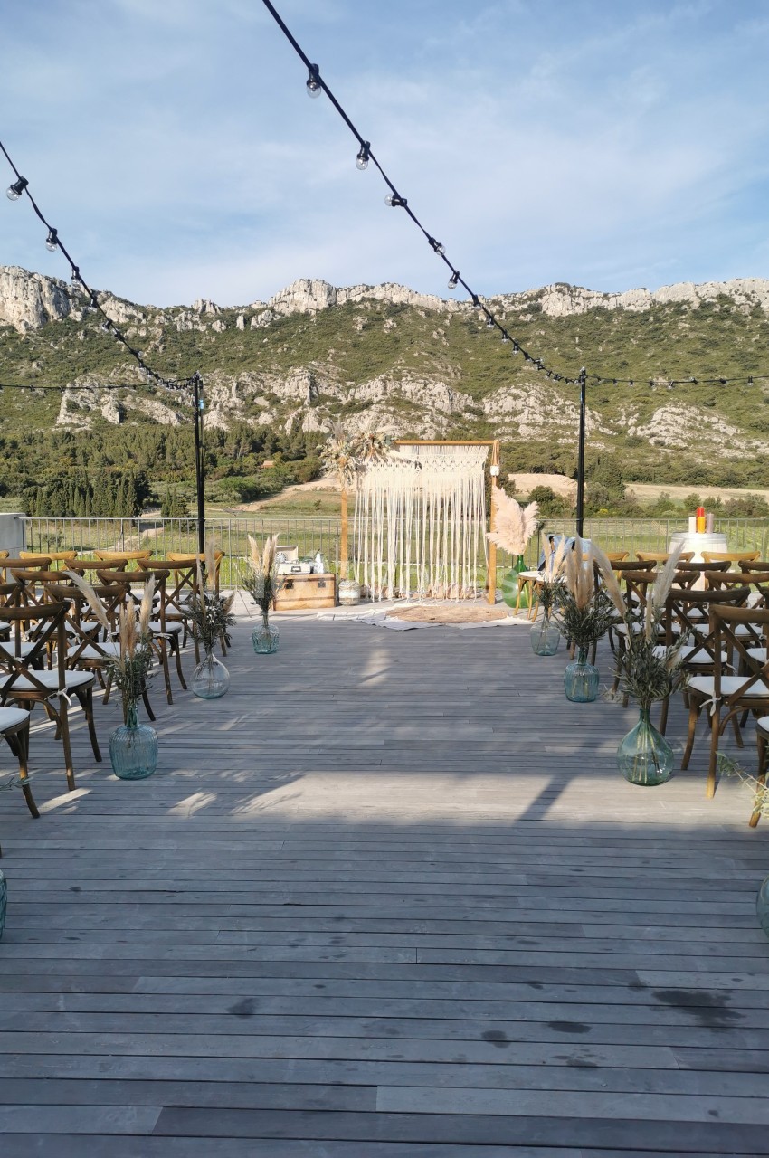 Allée en bois décorée pour une cérémonie en plein air, avec des chaises, des fleurs et une arche devant un paysage…
