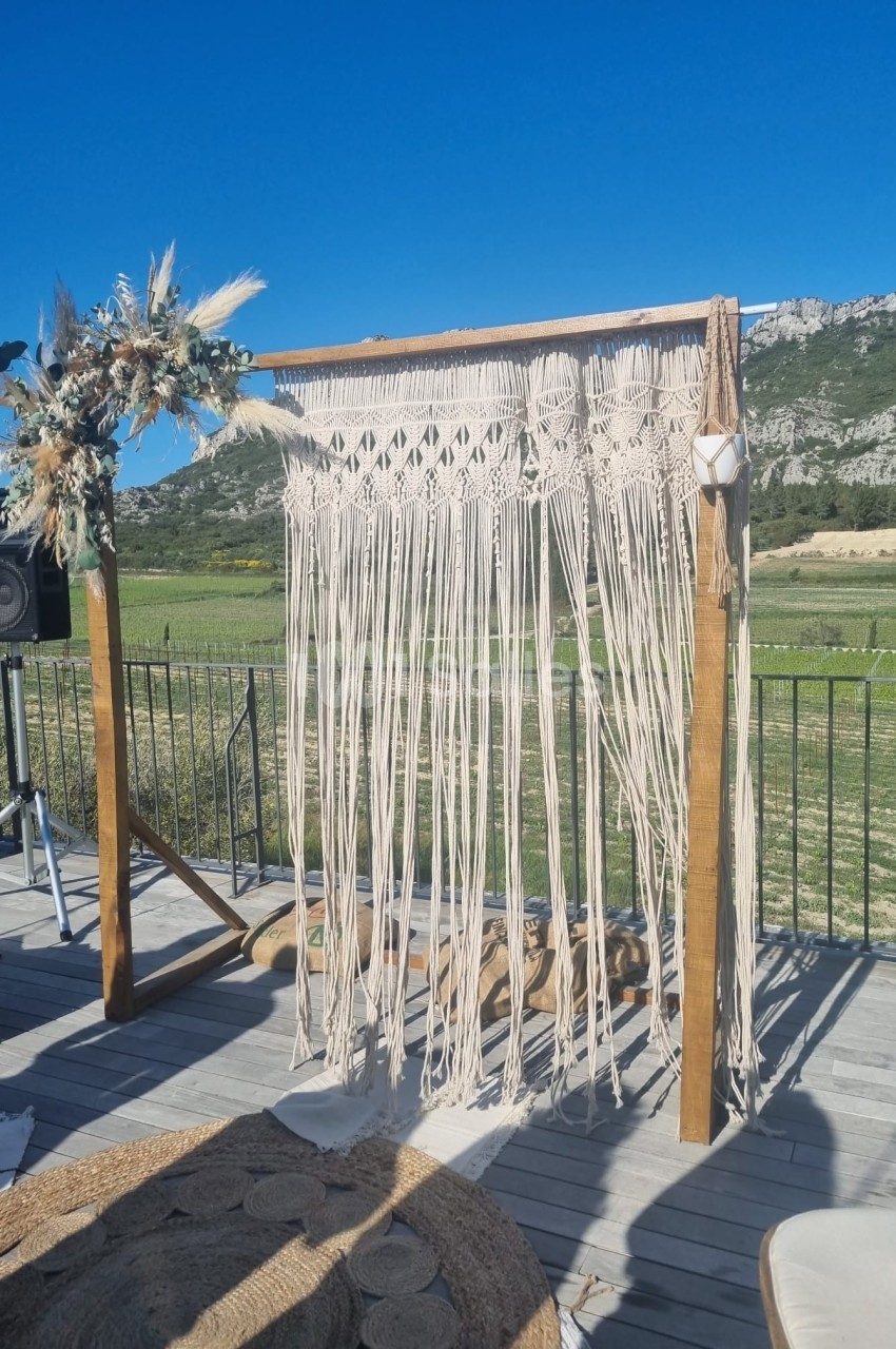 Arche en bois décorée de macramé et de fleurs séchées, installée en extérieur avec vue sur des montagnes.
