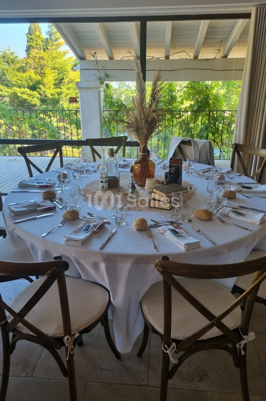 Table ronde dressée pour un repas, décorée avec des livres, un bouquet de fleurs séchées et des couverts disposés.