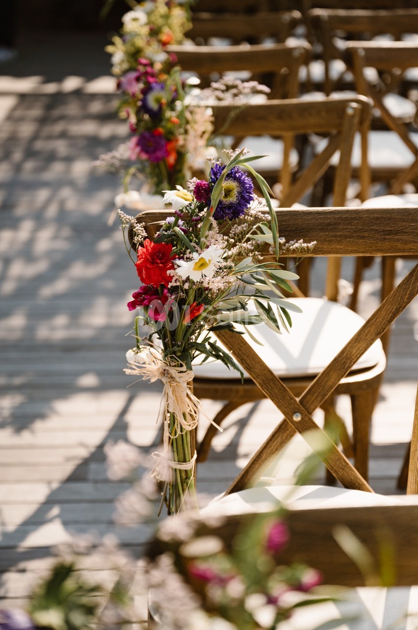 Chaises en bois décorées de bouquets de fleurs colorées, alignées sur une terrasse ensoleillée.