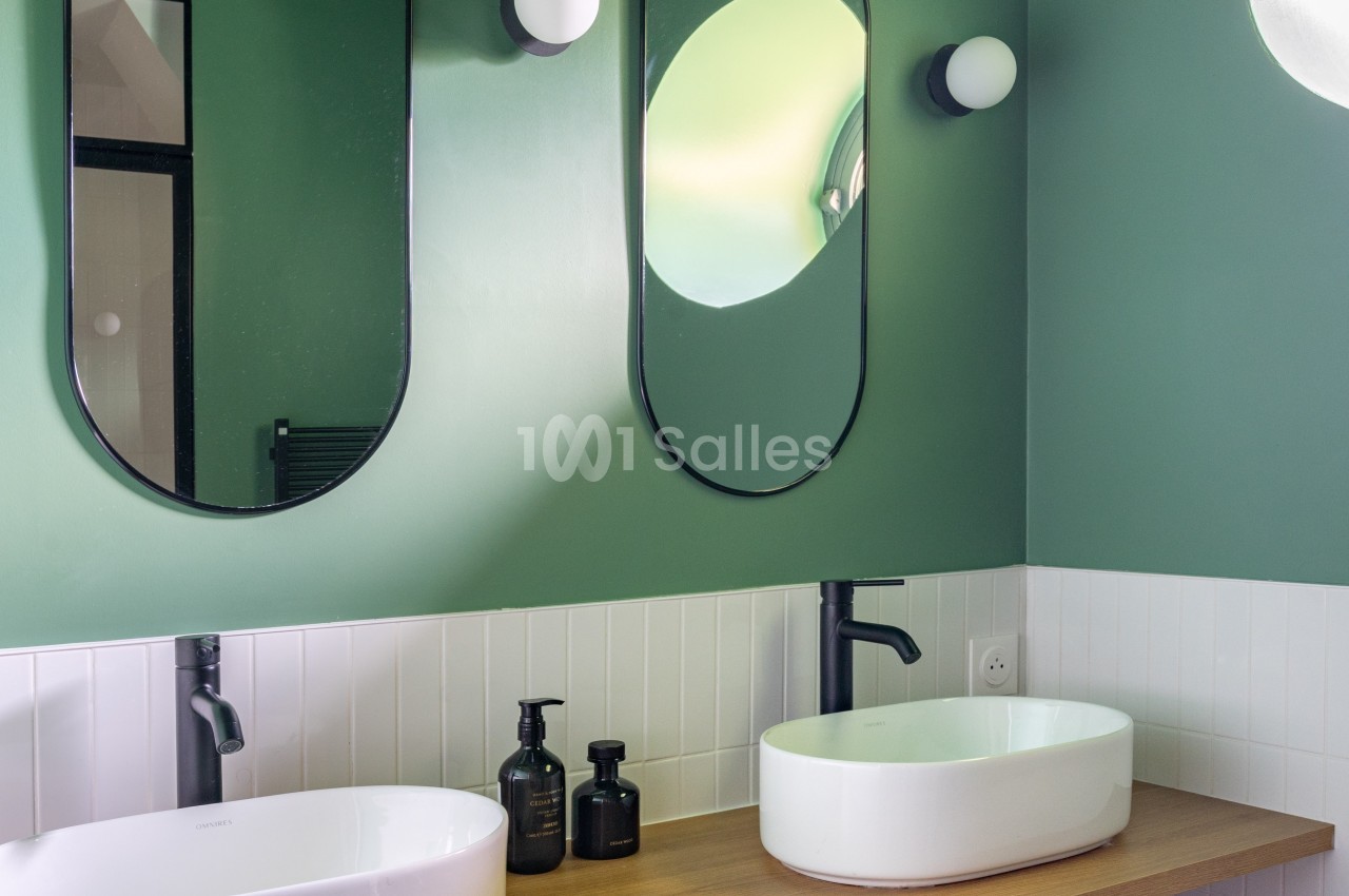 Salle de bain moderne avec murs verts, deux miroirs ovales, vasques blanches et plan de travail en bois.