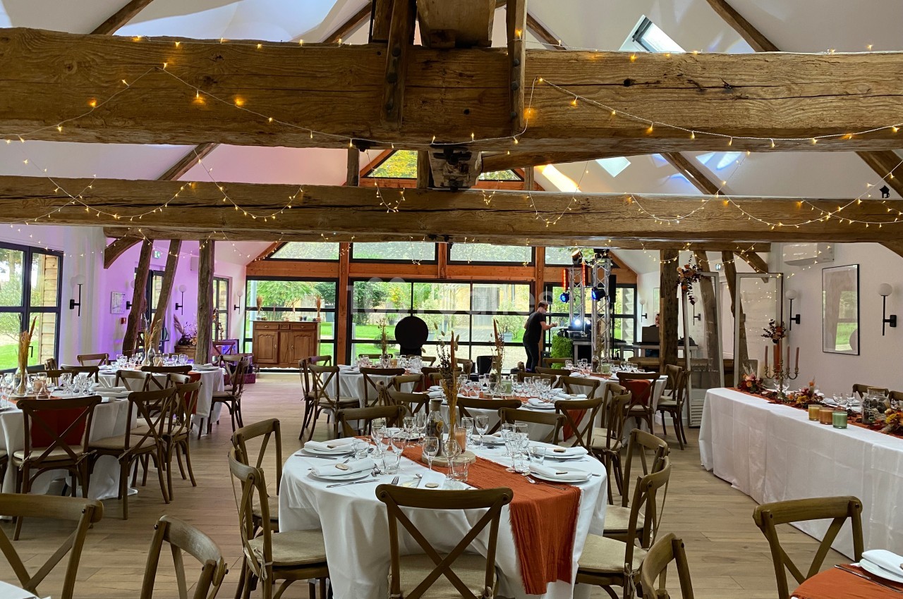 Salle de réception lumineuse avec poutres apparentes, tables dressées et décorations festives.