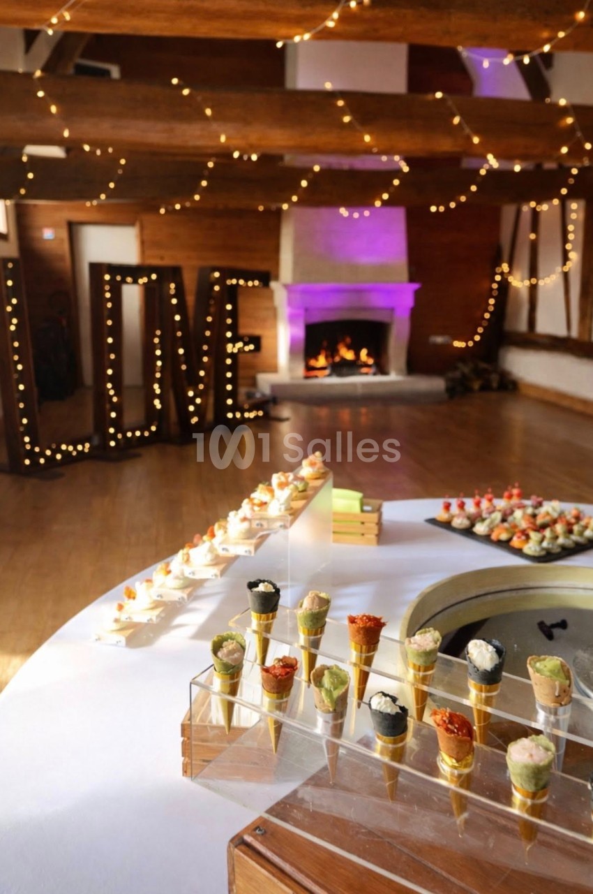 Buffet de réception avec cônes apéritifs, cheminée allumée et décor lumineux formant le mot ’LOVE’ en arrière-plan.