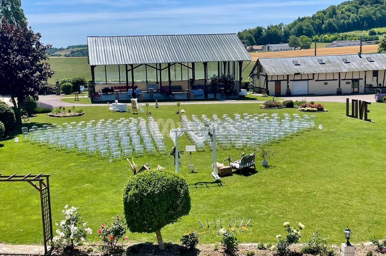 Chaises disposées en extérieur sur une pelouse pour une cérémonie, avec une arche décorée et un bâtiment en arrière-plan.