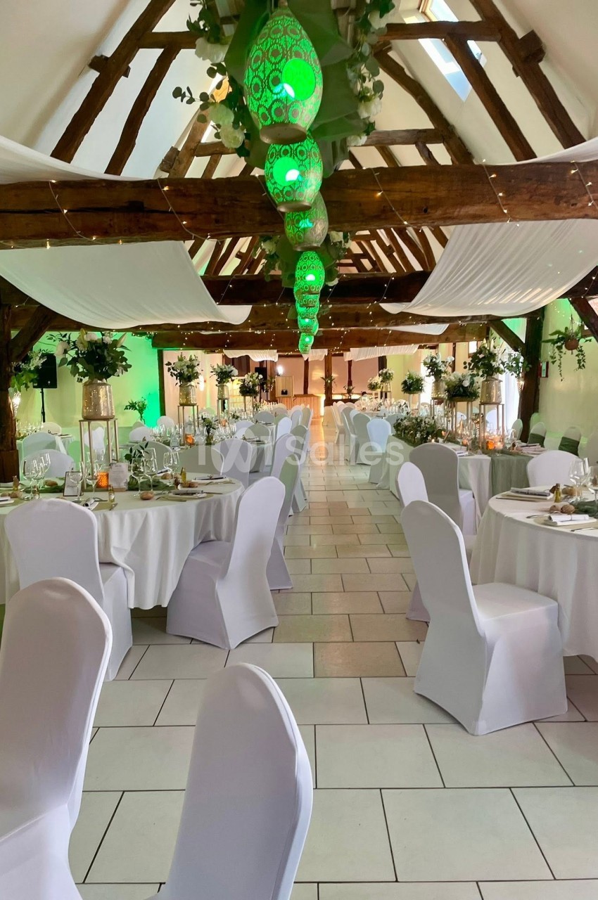 Salle de réception décorée avec des tables rondes, chaises blanches et lanternes vertes suspendues au plafond en bois.