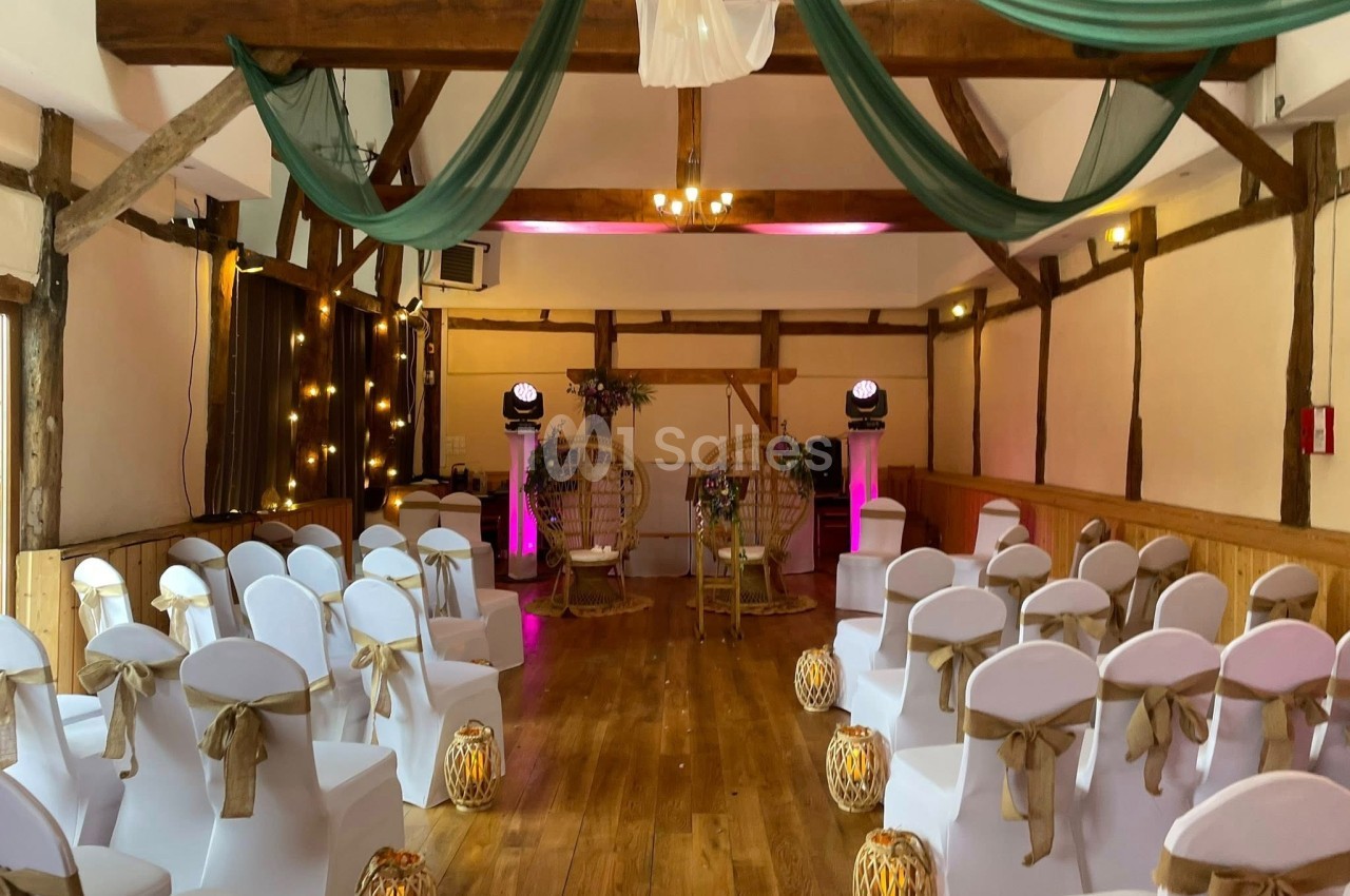 Salle de réception décorée pour un mariage, avec chaises blanches, lanternes au sol et drapés verts suspendus.