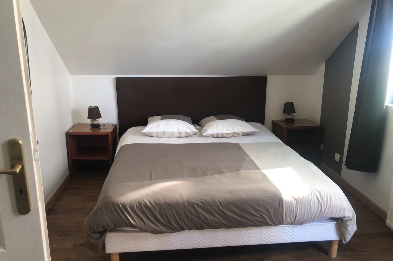 Lit double avec tête de lit sombre, draps gris et blancs, encadré par deux tables de chevet avec lampes, dans une chambre…