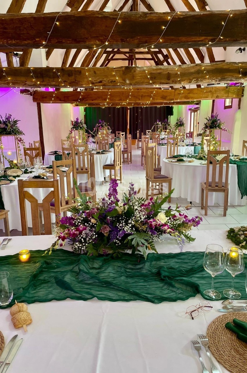 Salle de réception décorée avec des tables rondes, nappes blanches, chemins de table verts et compositions florales.