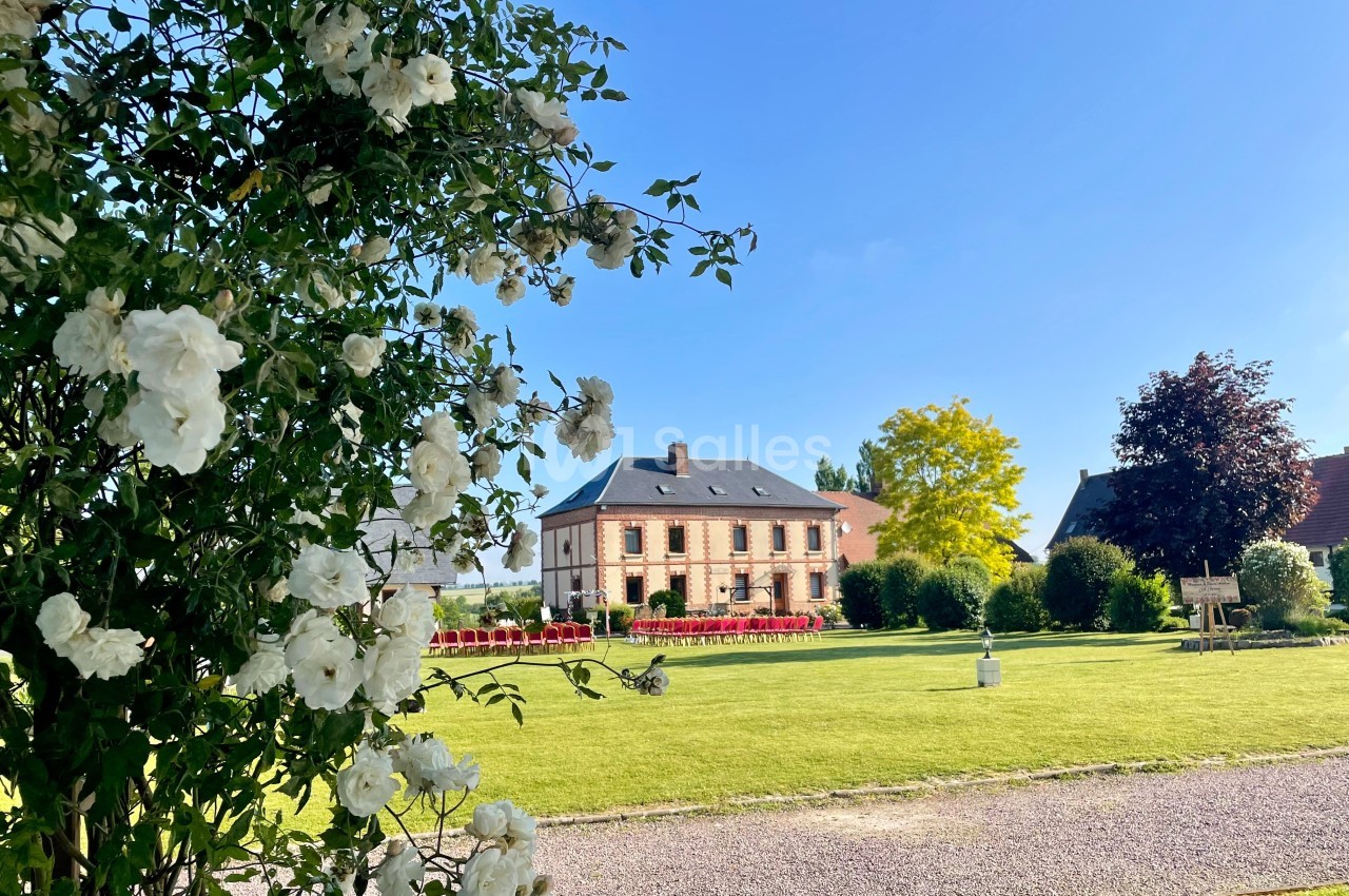 Vue d'une maison en briques entourée d'un jardin verdoyant, avec des fleurs blanches au premier plan.