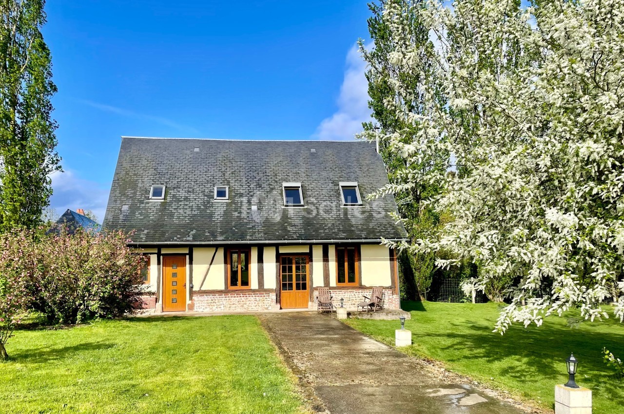 Maison à colombages entourée d'arbres en fleurs et d'une pelouse, avec une allée pavée menant à l'entrée.