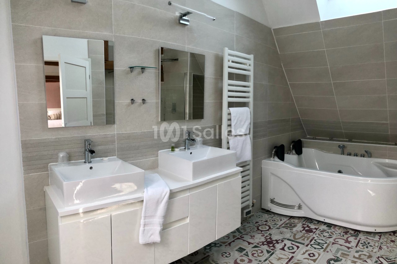 Salle de bain moderne avec double vasque, baignoire d'angle, sèche-serviettes et carrelage décoratif au sol.