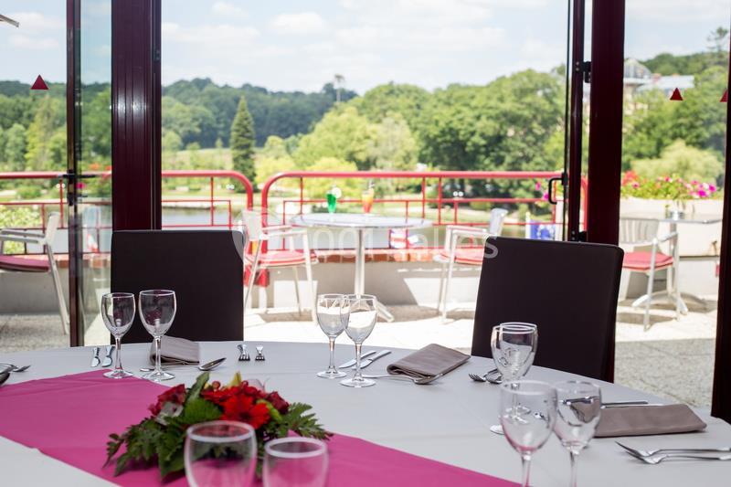 Table dressée avec nappe blanche, chemin de table rose, verres et couverts, donnant sur une terrasse avec vue sur un paysage…