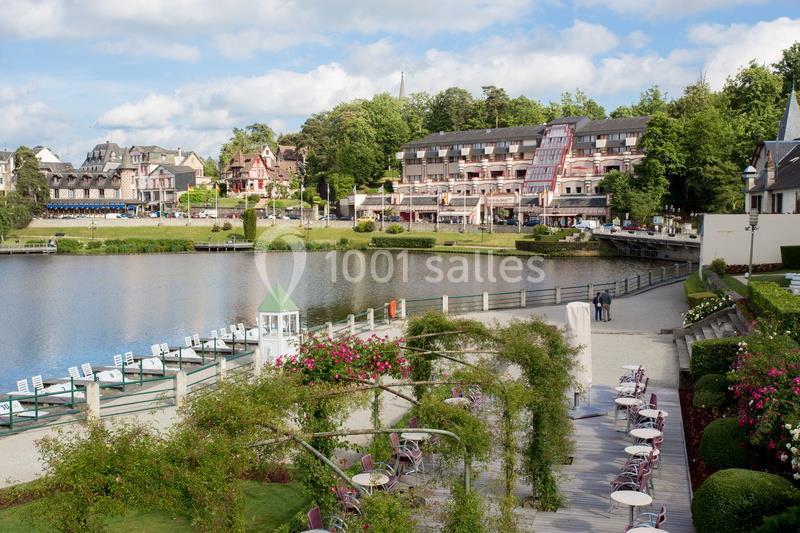 Vue sur un lac bordé de bâtiments, avec une promenade aménagée, des terrasses et des chaises longues au premier plan.