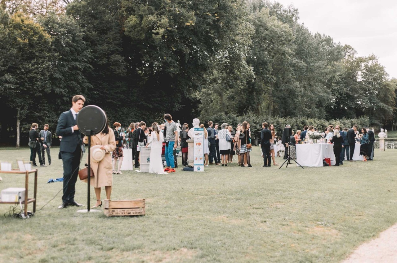 Groupe de personnes rassemblées dans un parc pour un événement, avec des stands et des tables en arrière-plan.