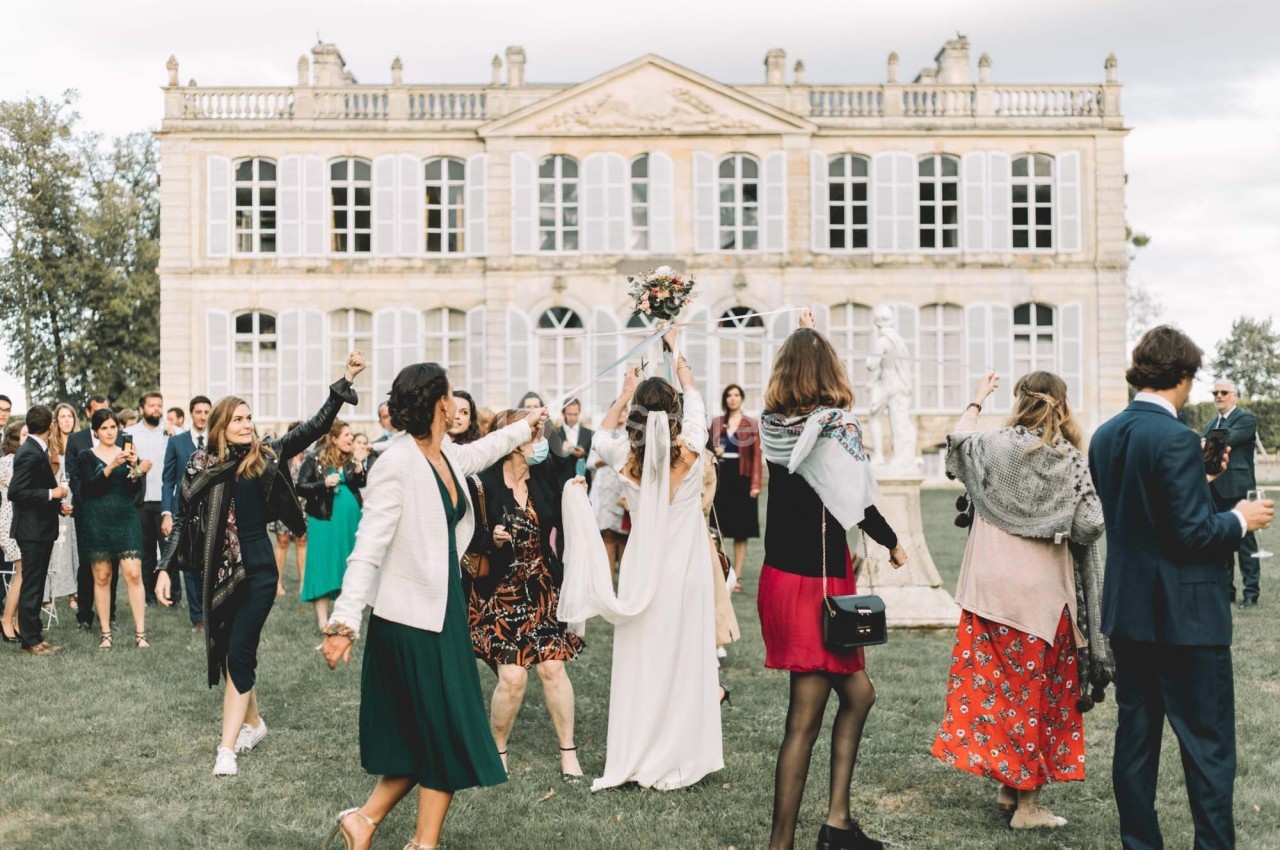 Un groupe de personnes célèbrent un mariage devant un grand bâtiment de style classique.