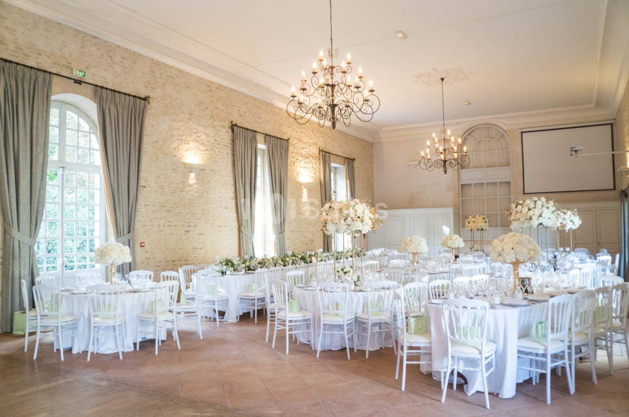 Salle de réception lumineuse avec tables rondes décorées de nappes blanches et compositions florales élégantes.