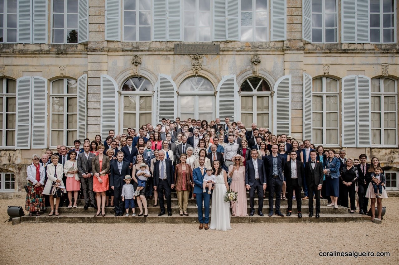 Groupe de personnes posant devant un bâtiment ancien avec des fenêtres à volets blancs.