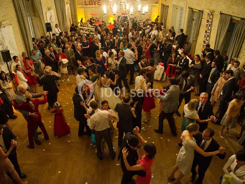 Groupe de personnes dansant dans une grande salle éclairée, décorée pour une réception festive.
