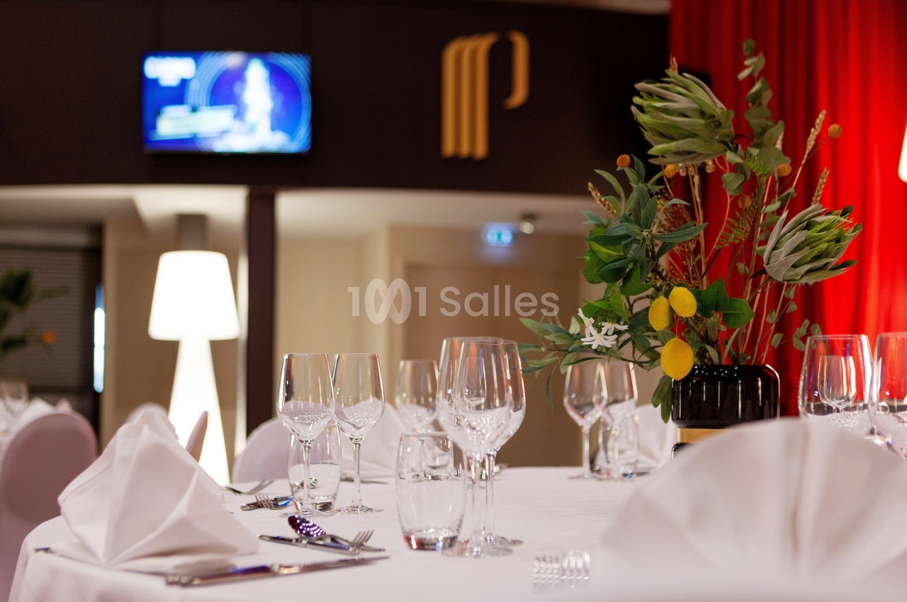 Table dressée avec nappes blanches, verres et serviettes pliées, décorée d'un bouquet floral dans une salle élégante.