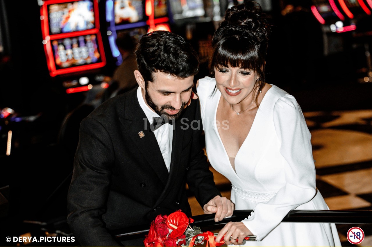 Un couple élégant joue à une machine à sous dans un casino, entouré de lumières et d'écrans colorés.