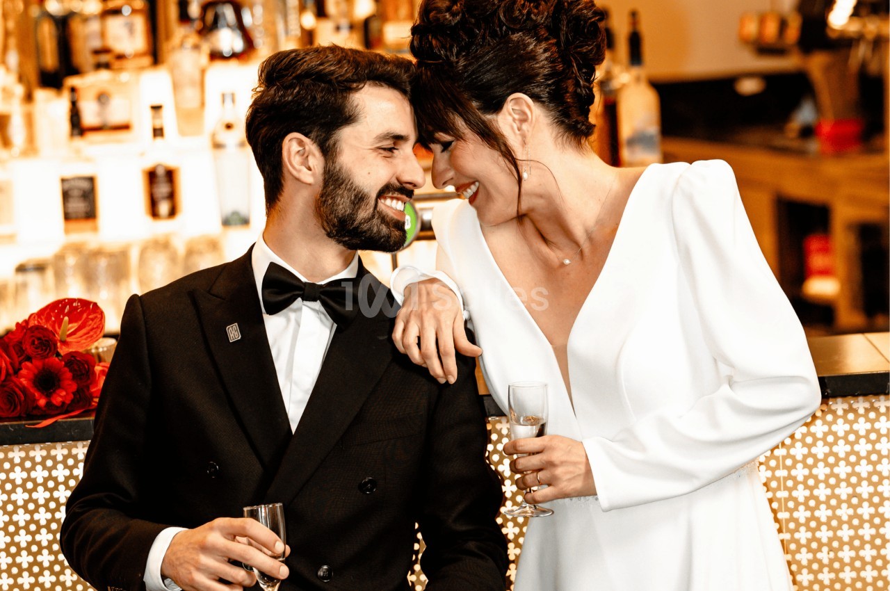 Un couple élégant souriant et partageant un moment complice devant un bar décoré avec des fleurs rouges.