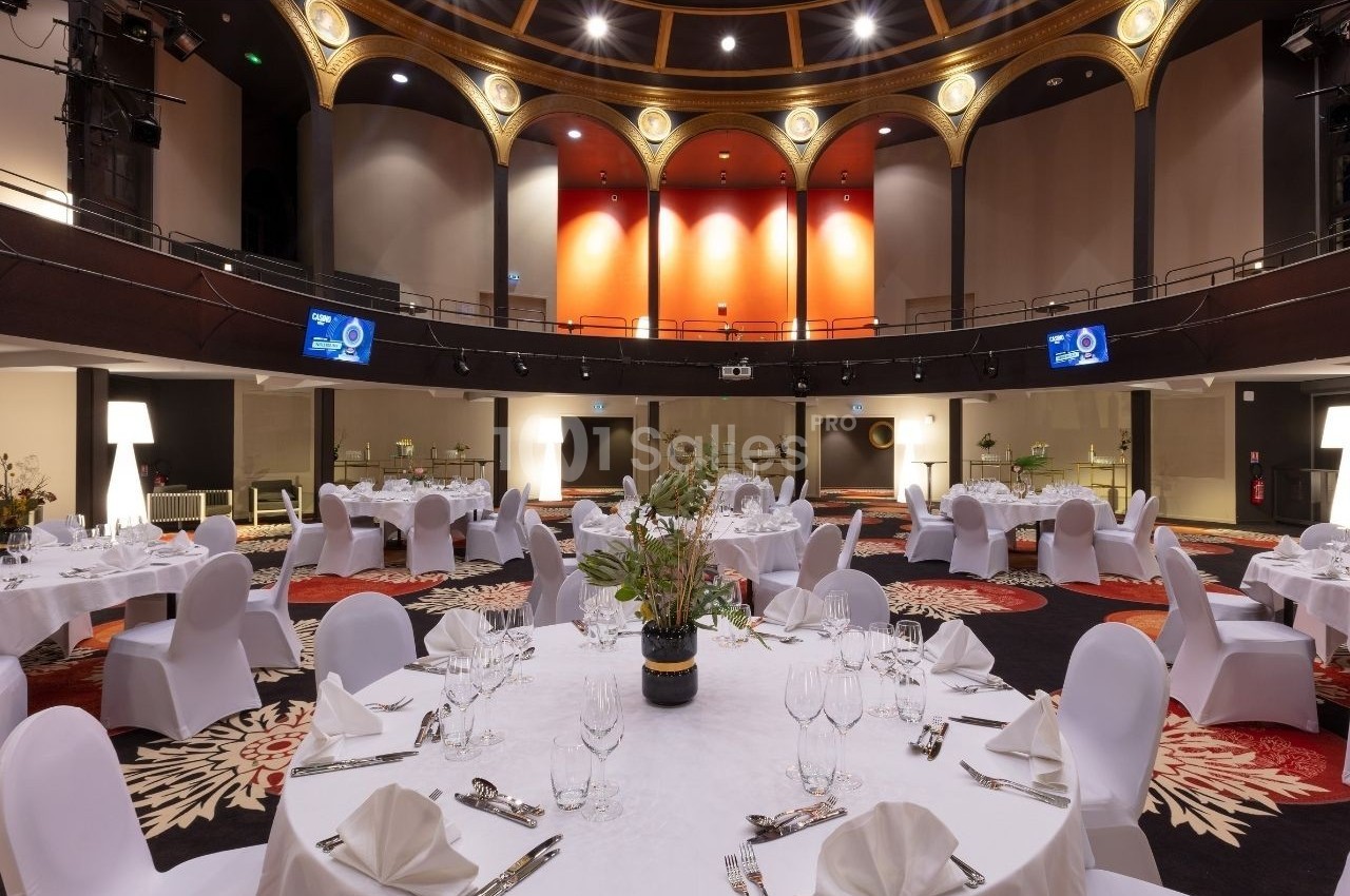 Salle de réception élégante avec tables rondes dressées, nappes blanches et décorations florales, sous un plafond voûté.