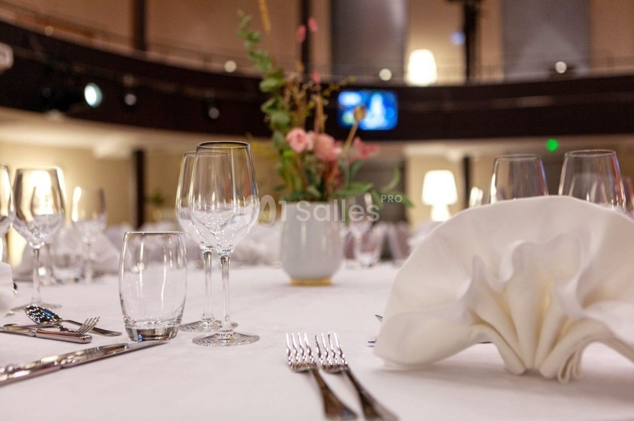 Table élégamment dressée avec verres, couverts, serviette pliée et vase de fleurs au centre, dans une salle éclairée.