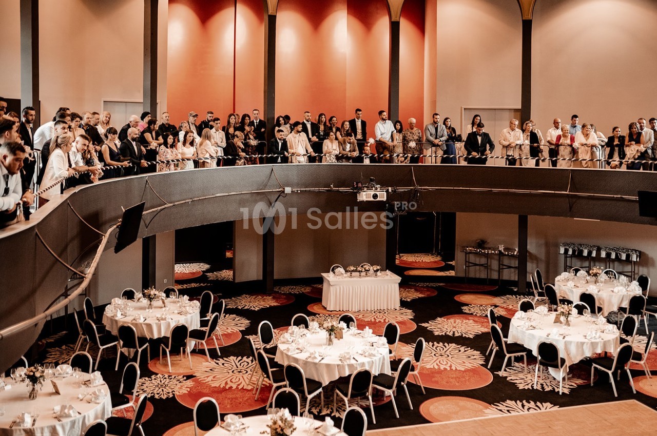 Salle de réception avec tables dressées en bas et un groupe de personnes debout sur une mezzanine.