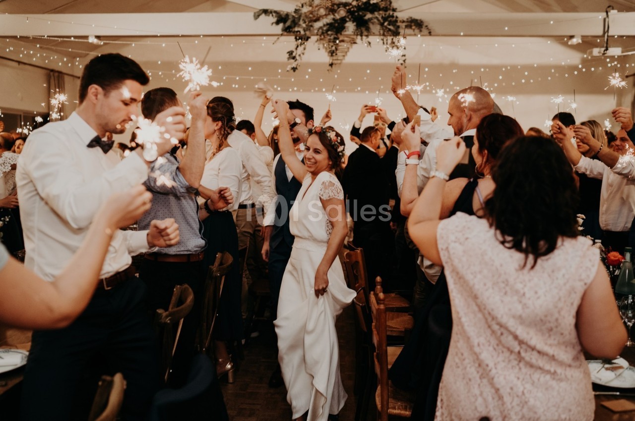Des invités célèbrent un mariage dans une salle décorée, tenant des cierges magiques allumés.