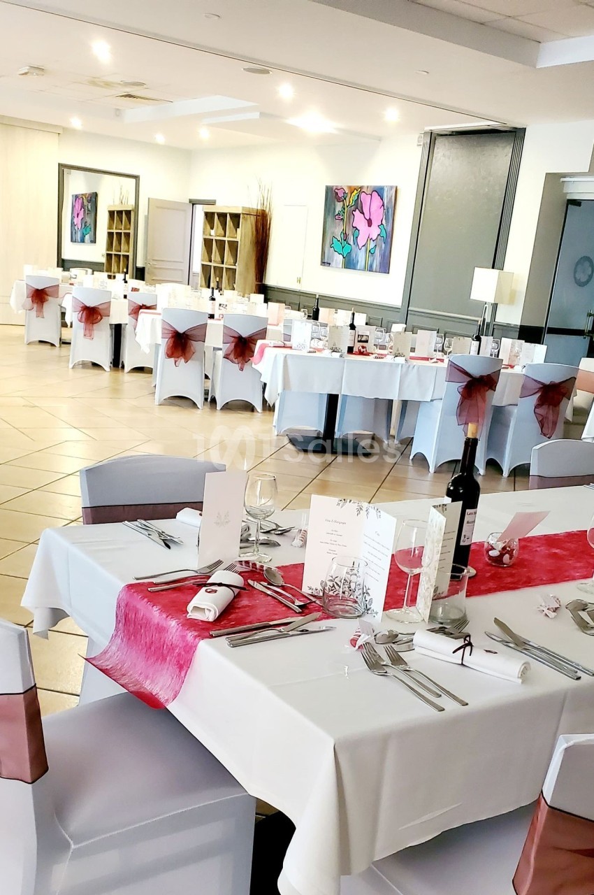 Salle de réception élégamment décorée avec des tables dressées, nappes blanches et chemins de table roses.