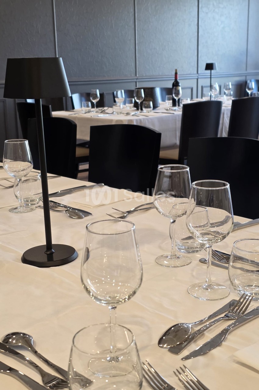 Tables de restaurant élégamment dressées avec nappes blanches, verres, couverts et lampes noires.