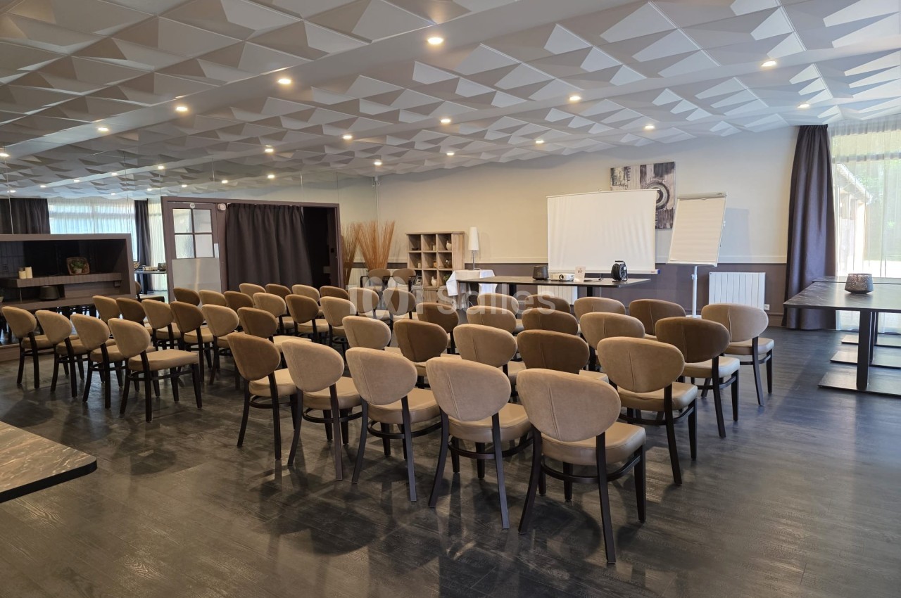 Salle de conférence lumineuse avec chaises alignées, écran de projection, tableau blanc et décor moderne.